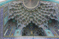 Ornate vaulted ceiling at the Shah Mosque in Isfahan, covered with symmetrical geometric and floral tilework in turquoise, blue, yellow and orange.