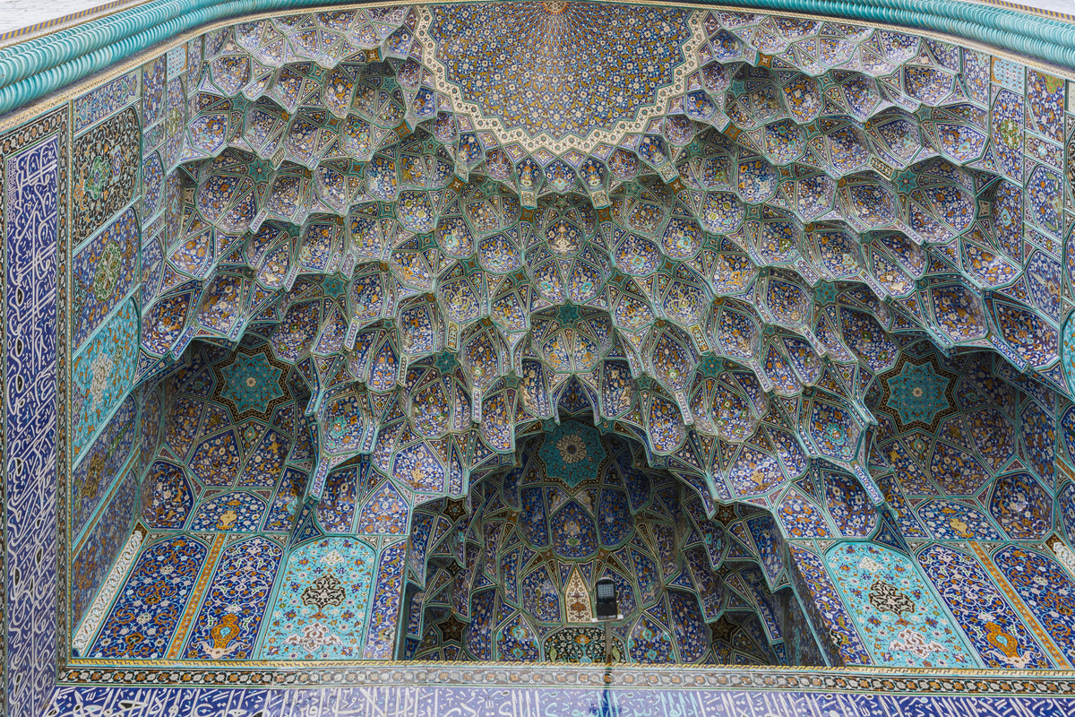 Ornate vaulted ceiling at the Shah Mosque in Isfahan, covered with symmetrical geometric and floral tilework in turquoise, blue, yellow and orange.