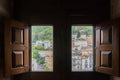 Open wooden shutters frame two tall windows overlooking the tiled rooftops and green hillside of Sintra from inside the National Palace.